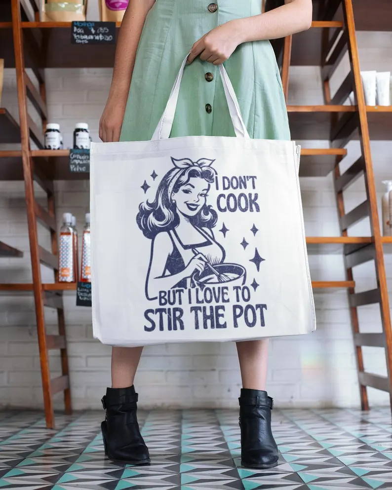 Featured Retro Humor tote bag mockup: a 1950s housewife illustration with dark blue typography and the snarky quote 'I Don't Cook But I Love To Stir The Pot